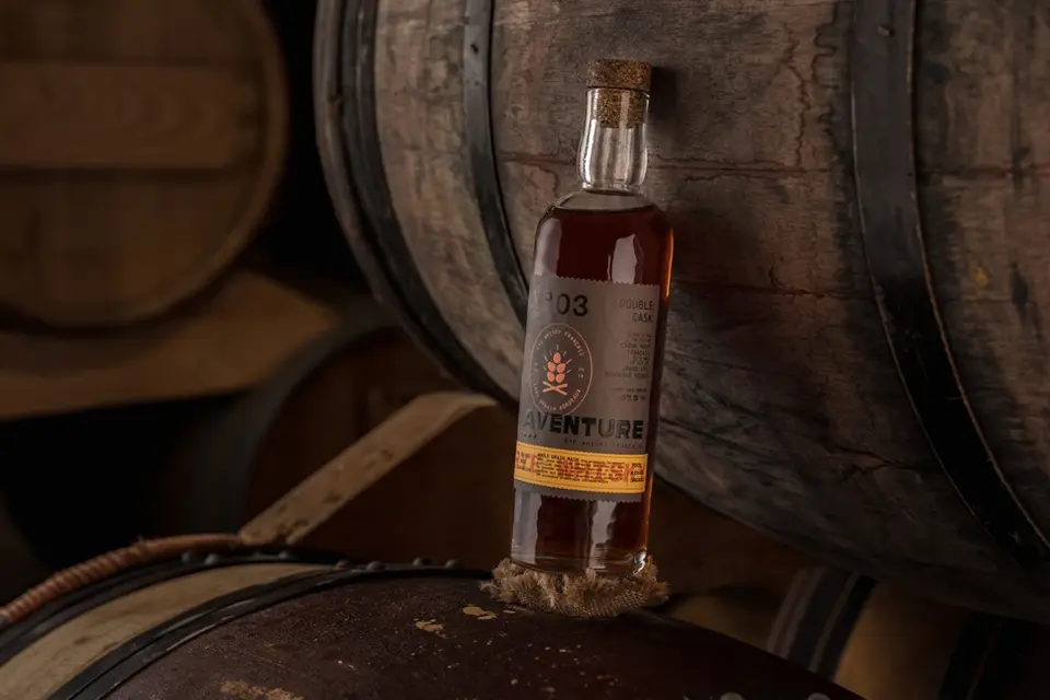 L’étiquette de la bouteille de whisky rye Aventure, présentée entre des tonneaux, a été réalisée par Autajon Étiquettes Atlantique