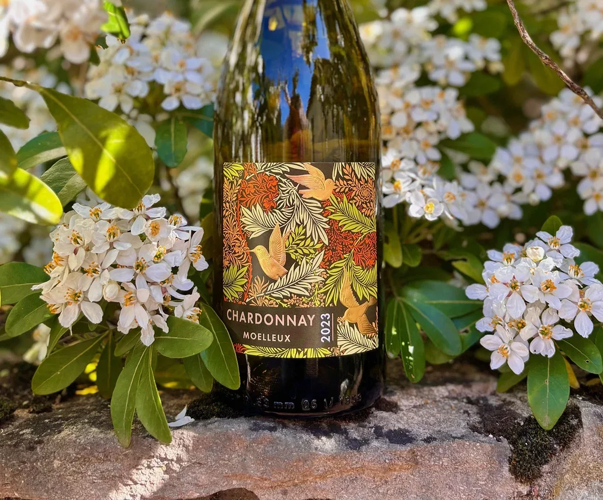 L’étiquette de la bouteille de vin blanc, mise en scène dans un décor fleuri et naturel, a été conçue par Autajon Étiquettes Bourgogne.